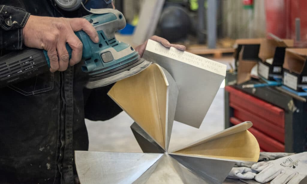 Artisan polishing a custom bronze trophy during production at the Capa Esculturas art foundry in Madrid.<br>