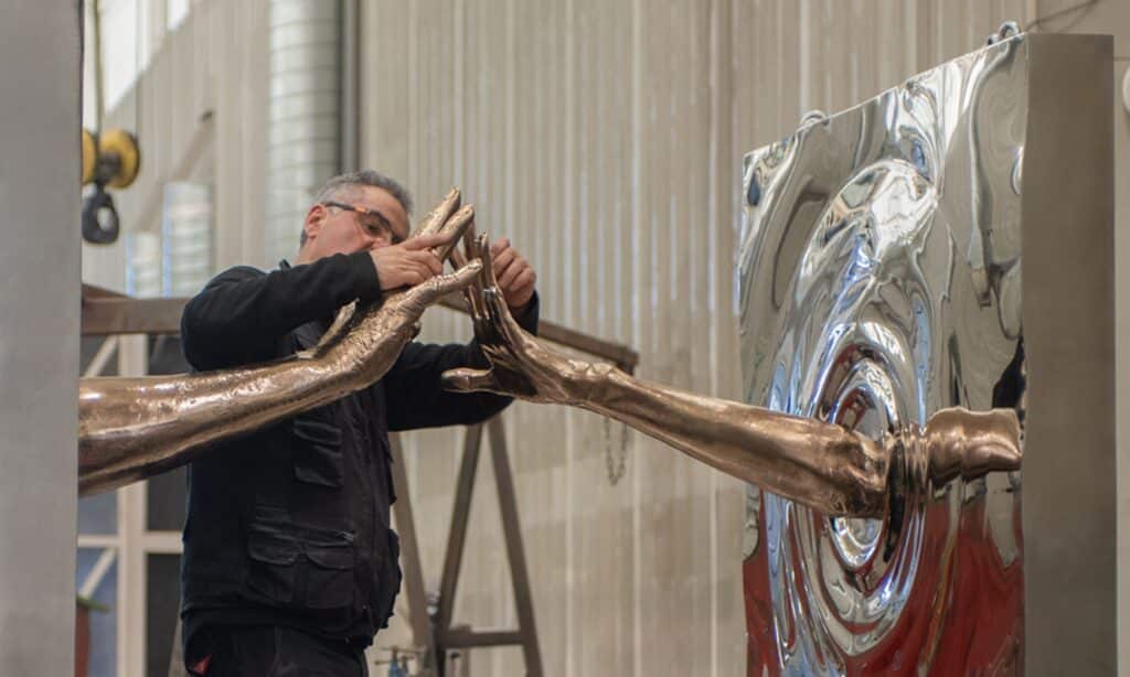 Sculptor working on bronze and steel sculpture with certified authenticity.