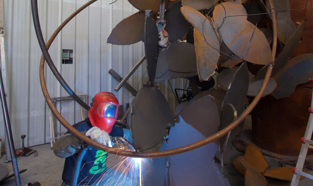 Worker welding a metal structure during the creation of a contemporary monumental sculpture