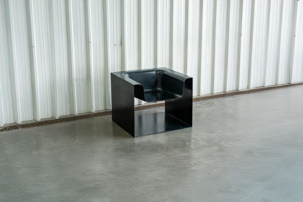 Detalle lateral de la escultura “Meteoro” con acabado metálico y líneas continuas.