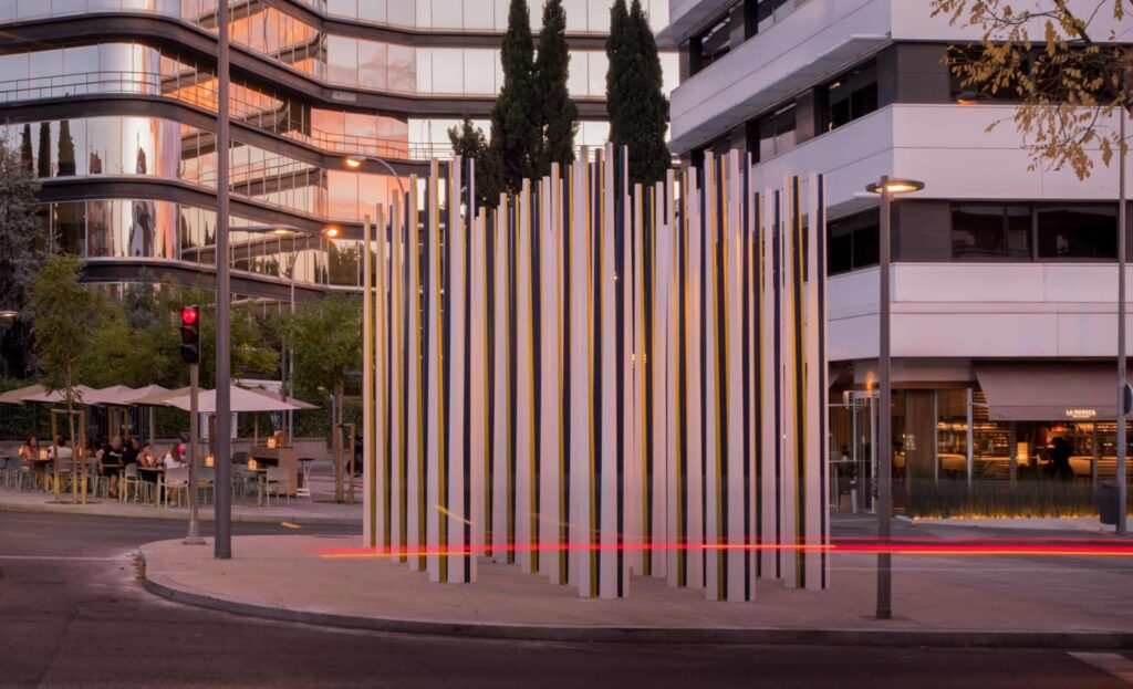 Escultura "Recuerdo Vivo" iluminada por la luz del atardecer, rodeada de edificios modernos en Chamartín, Madrid.