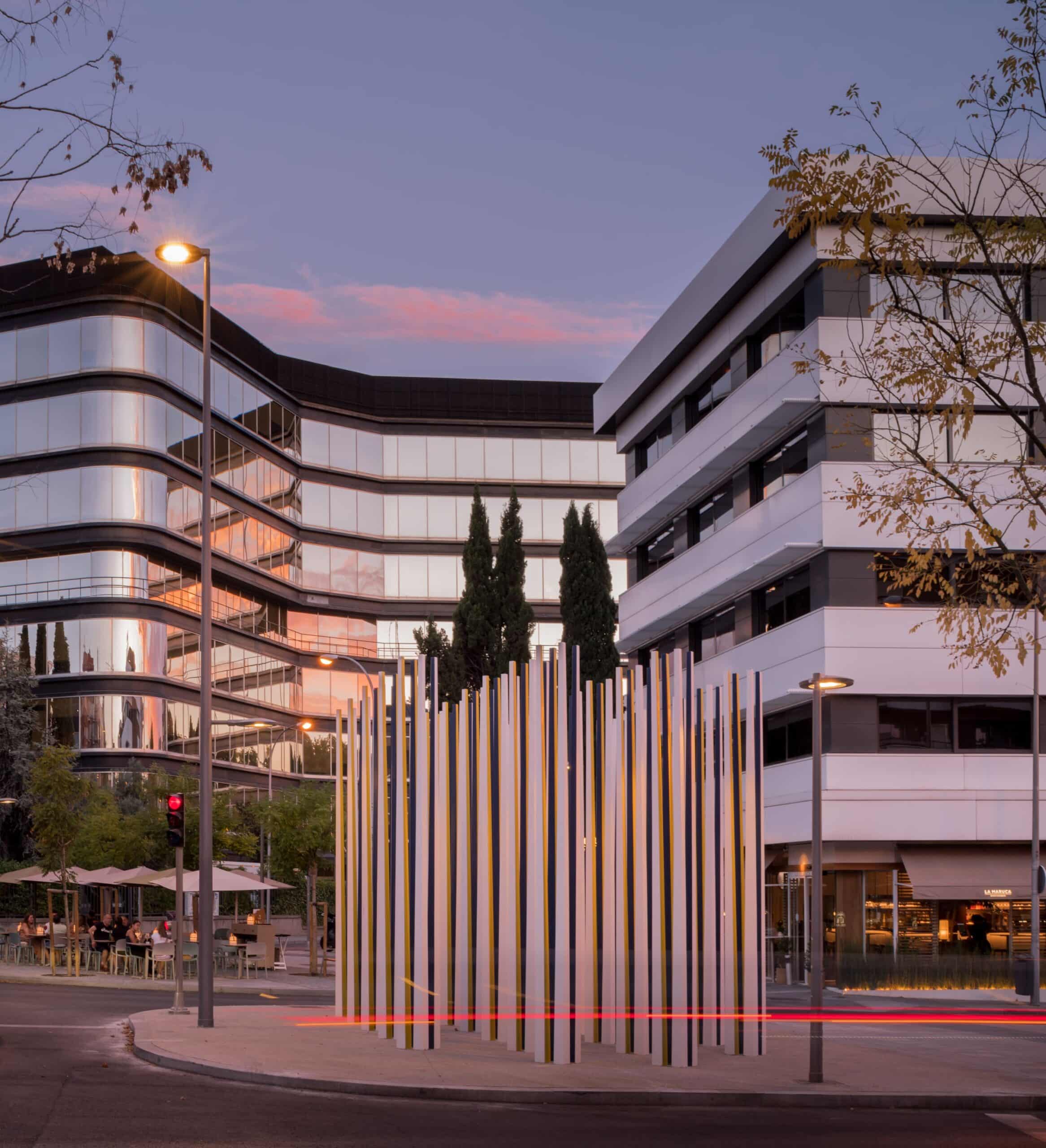 The sculpture “Living Memory” captured at sunset, with the light highlighting the prisms and modern buildings in the background.