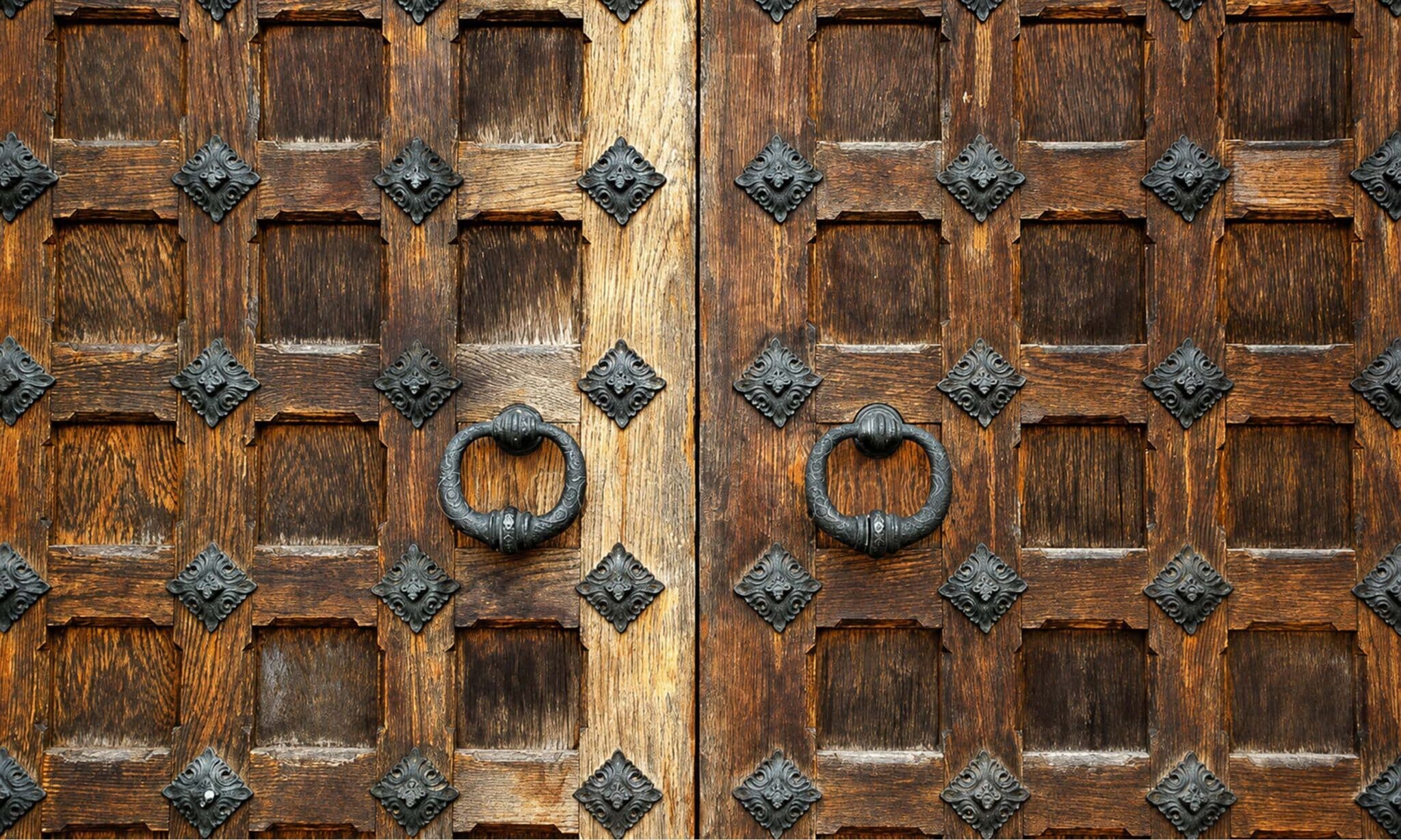 Puerta de madera antigua con dos aldabas de metal y herrajes decorativos tradicionales.
