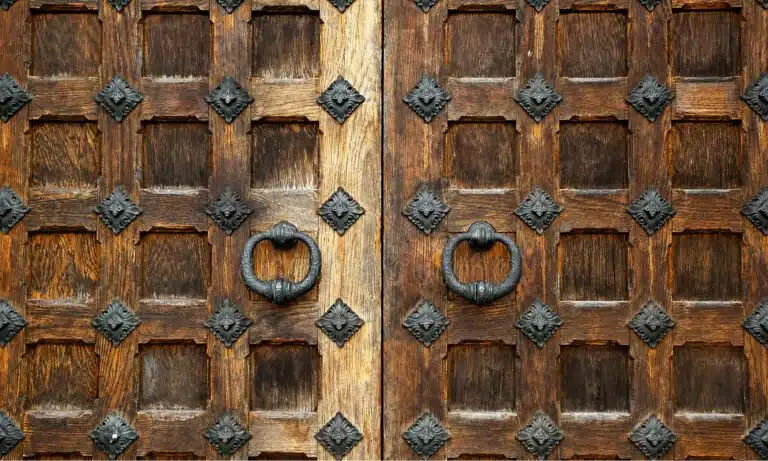 Puerta de madera antigua con dos aldabas de metal y herrajes decorativos tradicionales.
