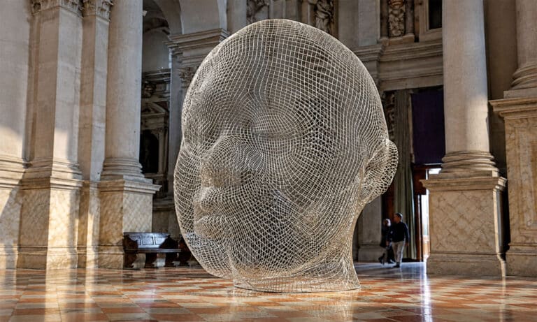 Escultura de Jaume Plensa con forma de cabeza humana realizada en malla metálica, expuesta en el interior de un edificio histórico.