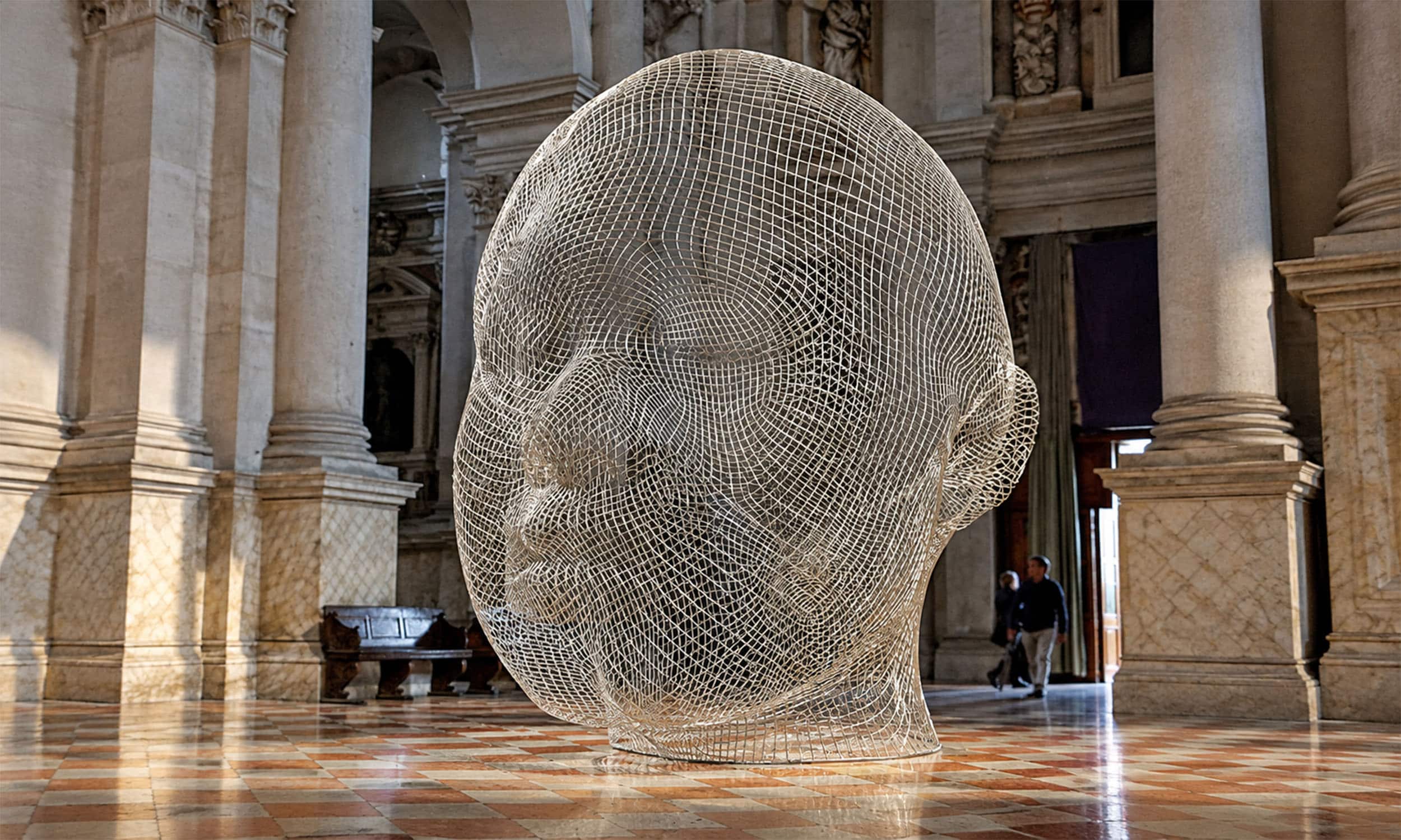 Escultura de Jaume Plensa con forma de cabeza humana realizada en malla metálica, expuesta en el interior de un edificio histórico.