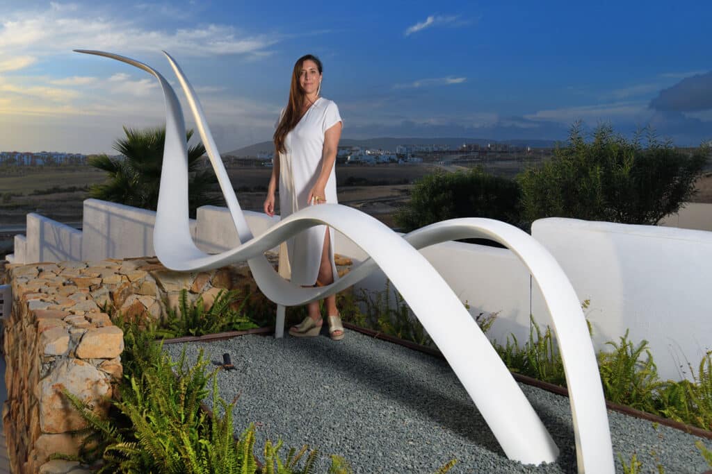 Verónica Mar detrás de su escultura "Roma Past" en un entorno verde y natural