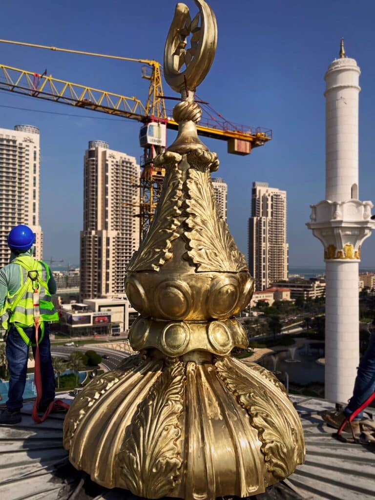 Operator next to a newly installed bronze Pinnacle at the Hamad bin Jassim Mosque, with the Doha skyline in the background.