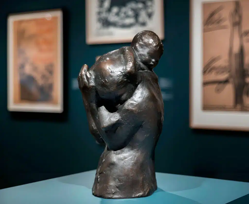Escultura expresionista de Käthe Kollwitz Maternidad, Dolor y Resistencia, con figuras humanas abrazadas reflejando pérdida y resiliencia.