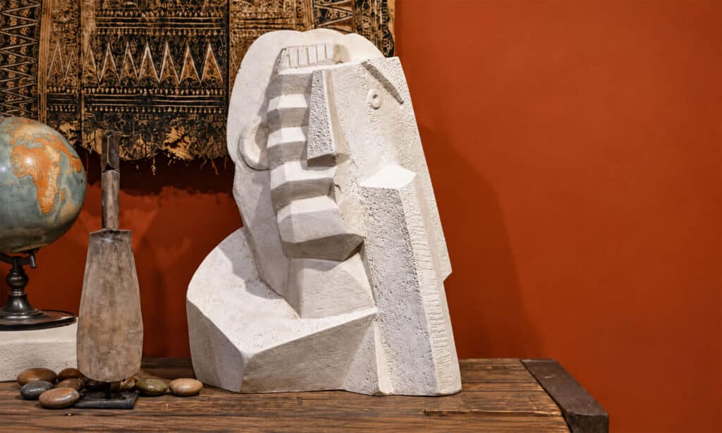 A Cubist sculpture of a human face with geometric planes and fragmented volumes on a wooden table.